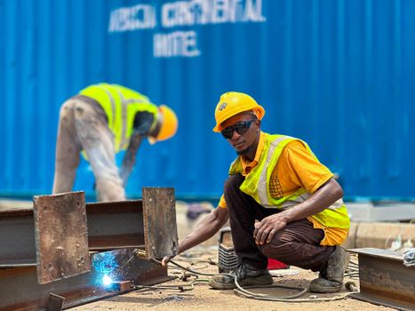 Construction workers welding steel beams outdoors, wearing safety gear.