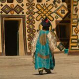 A person in traditional attire walks past a vividly painted building in an African village. Cultural immersion.