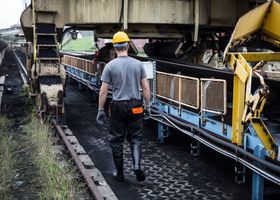A worker in safety gear examines industrial machinery in an outdoor setting, showcasing industry work.