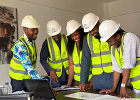 Diverse team of African engineers in hard hats and safety vests reviewing building plans indoors.