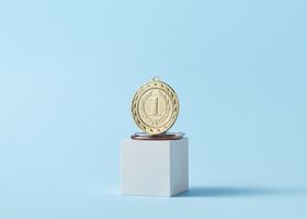 Close-up of a gold medal on a podium with a baby blue background, symbolizing victory.